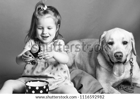child is playing with the dog. Happy little girl with smiling funny face playing with plastic car toy near labrador dog pet in studio on grey background