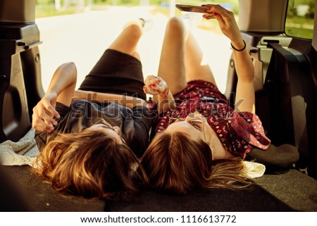 Two girls lying down in the trunk and taking selfie.