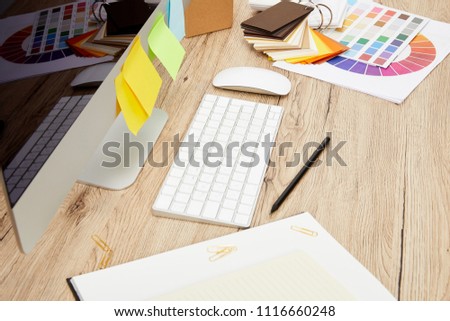 close up view of designer workplace with computer screen with colorful stickers, notebooks and pallet on wooden tabletop