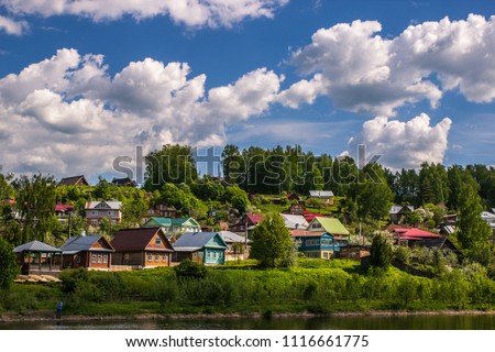 the landscape of a Russian village in summer with colorful houses and a blue sky with huge white clouds, a rustic background Royalty-Free Stock Photo #1116661775