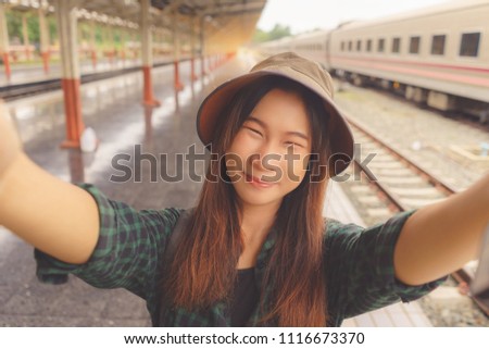 Asian young girl holding camera and making selfie and smiling at train station.
