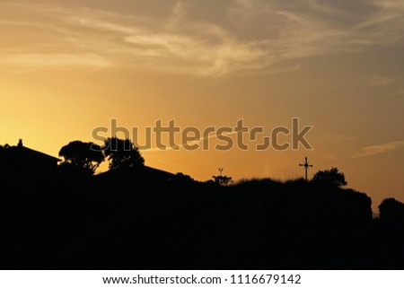 A golden sunset over the city hills with a cross and roofs