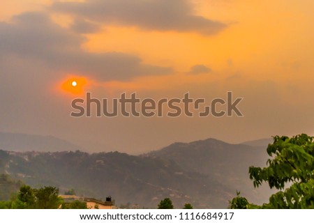 Landscape Photograph of vibrant color dramatic cloudy overhead sky over mountain at sunset with tree leaves in foreground.