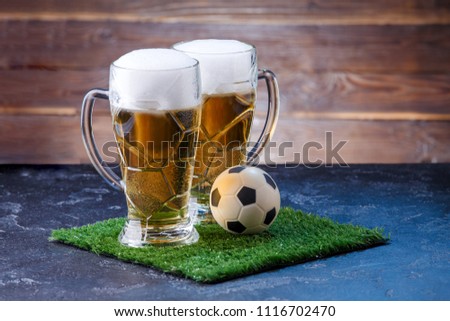 Photo of two glasses of beer, soccer ball on green grass at table