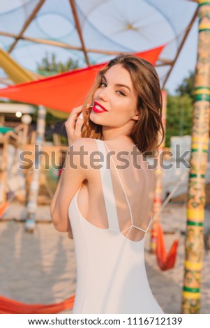 Portrait from back of elegant young european woman in white swimsuit having fun at beach. Lovely girl looking over shoulder and playing with her shiny hair.