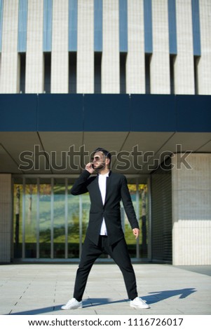 A successful representative a rich and fashionable man with a beard standing on the street in front of modern building. On men sunglasses.