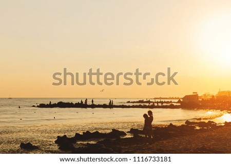 Summer sea landscape with sunset, orange clean sky, seagulls and people. Silhouettes of two little girls are on the background of the sea. Concept of tourism, summer family vacation. Free space.