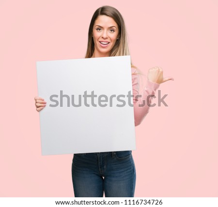 Beautiful young woman holding advertising banner pointing with hand and finger up with happy face smiling