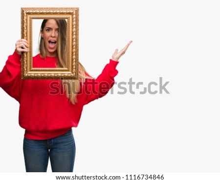 Beautiful young woman holding vintage frame very happy and excited, winner expression celebrating victory screaming with big smile and raised hands