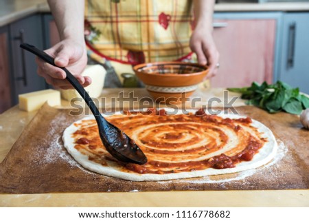Cooking pizza. the workpiece poured tomato sauce. Closeup hand of chef baker in uniform blue apron cook at kitchen
