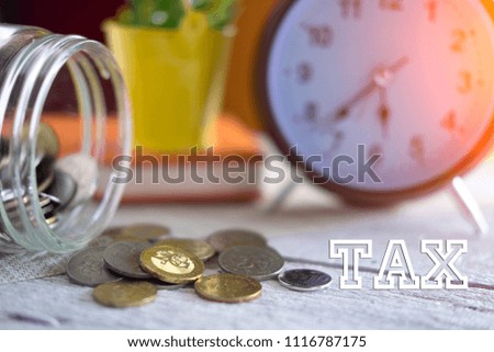 Time to pay TAX concept. TAX text with stack of coin and vintage alarm clock on wooden table in daylight background, business and financial concept idea. Selective focus