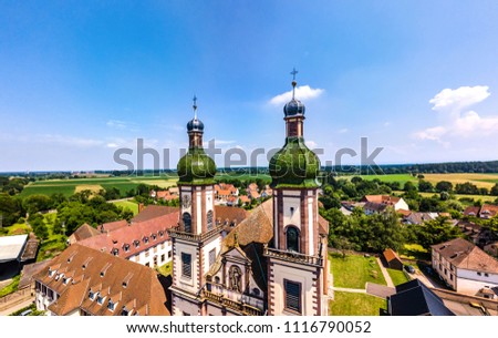 Soaring majestic church Saint Maurice in little french village Ebersmunster. Aerial drone view. Alsace. France. Royalty-Free Stock Photo #1116790052