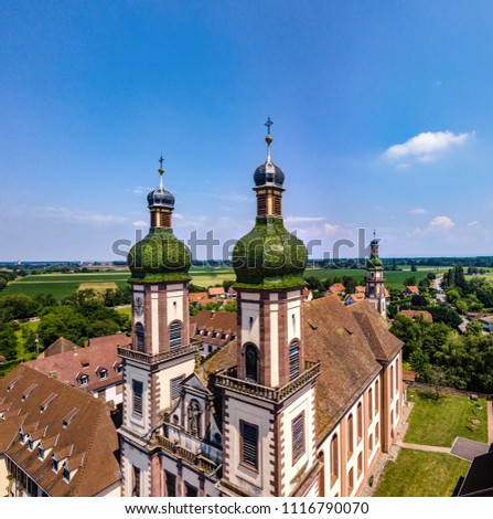 Soaring majestic church Saint Maurice in little french village Ebersmunster. Aerial drone view. Alsace. France. Royalty-Free Stock Photo #1116790070