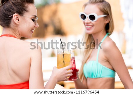 happy young women clinking glasses of cocktails at poolside
