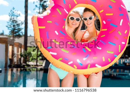 happy young women looking at camera through inflatable ring in shape of bitten donut at poolside
