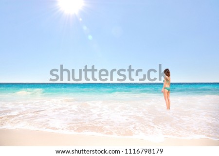 Beautiful woman in bikini standing and looking view of tropical beach ocean on hot summer day with blue sea and sunlight.Relaxing time on paradise.Vacation,Travel,Holiday and Day off Concept.