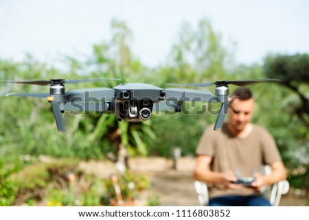 closeup of a caucasian man operating a drone, remotely controlled with a smartphone, in a natural landscape