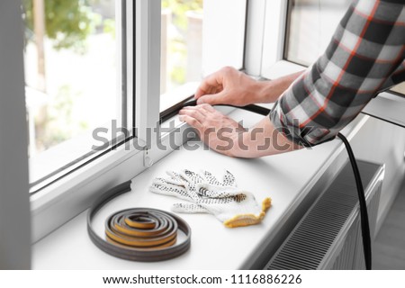 Young man putting sealing foam tape on window indoors Royalty-Free Stock Photo #1116886226