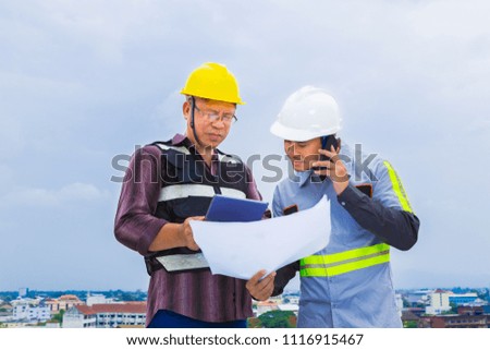 Asian construction engineer working with his foreman while using his cellphone at construction site, good for teamwork and engineering theme