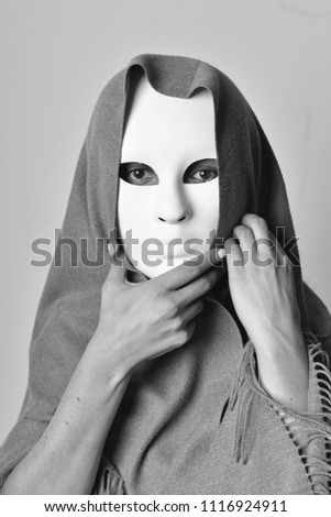 Black and white photo of a woman in a white mask and grey scarf, she looks reflectively and sadly 