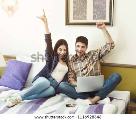 Happy couple shopping online on laptop while sitting on bed in hotel room