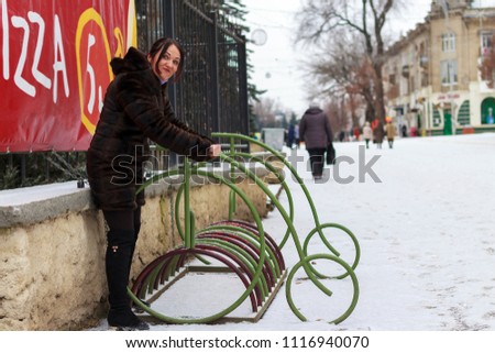 Girl grimaces in the bike Parking in winter, depicting Cycling