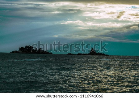 Sun setting between clouds above the wavy sea and islands