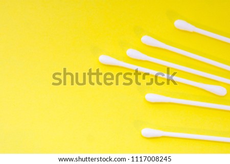 White cotton swabs or buds are on yellow uniform background view from above with clear area of half of photo for labels or headers. Hygienic products for cleaning ears, aural hygiene and cosmetics 