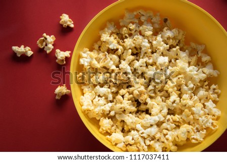 Tasty caramel popcorn in a yellow plate on the red background and next to the scattered pop corn, top view