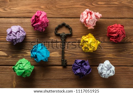 Set of multiple colorful crampled paper ball and key among them, placed on wooden table as means of searching of new ideas.