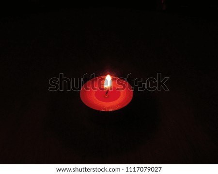 A small red tealight candle lit in a dark room on a table