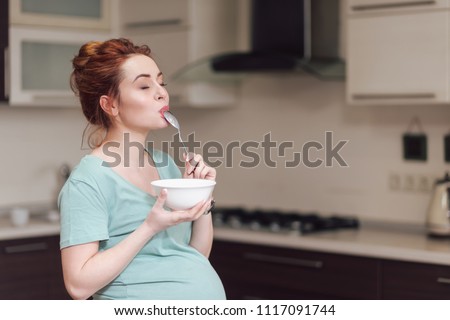 Beautiful pregnant woman eating with lust cereals on breakfast, enjoying meal. Yummy food for pregnant ladies Royalty-Free Stock Photo #1117091744