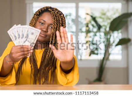African american woman holding dollars with open hand doing stop sign with serious and confident expression, defense gesture