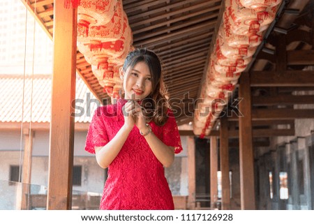 Portrait beautiful young woman wear cheongsam red dress with gesture of congratulation looking at camera in Chinese New Year Festivities. Celebration concept