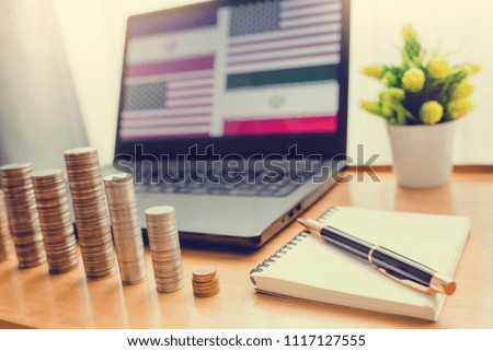 IRAQ VS USA flag in laptop background with front gold silver coins and notebook with pen. There are on wooden table. The concept of situation.
