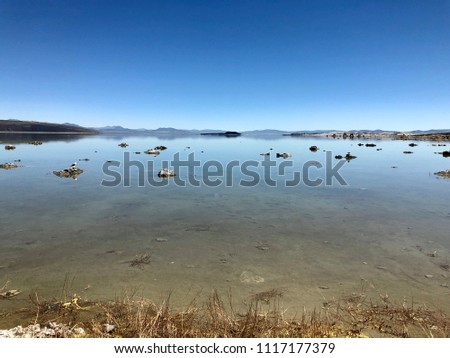Mono Lake, California- low angle including partial shore with sand and rocks, expanse of blue sky, shallow blue water, mountain range in distance