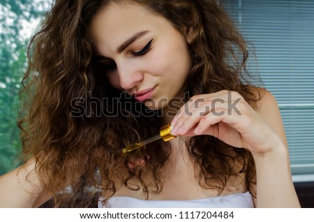 young beautiful curly woman uses yellow serum for hair. The concept of hair care.