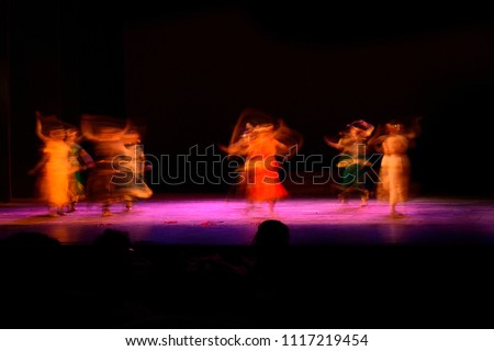 A group of people dancing on stage against black background. Photograph is taken with long expose.  