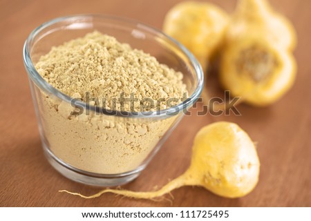 Maca powder (flour) in glass bowl with maca roots or Peruvian ginseng (lat. Lepidium meyenii) (Selective Focus, Focus one third into the maca powder) Royalty-Free Stock Photo #111725495