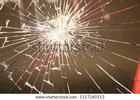 Close up outdoor view of a broken glass window. Abstract image of vandalism and damage. Pattern of lighted lines on a transparent surface with a dark background. 