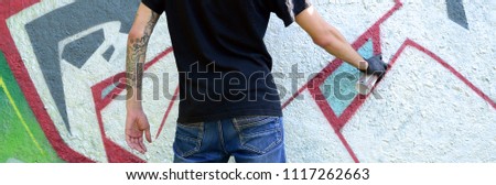 A young hooligan paints graffiti on a concrete wall. Illegal vandalism concept. Street art