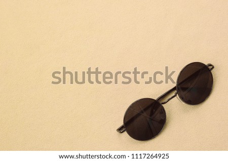 Stylish black sunglasses with round glasses lies on a blanket made of soft and fluffy light orange fleece fabric. Fashionable background picture in fashion colors