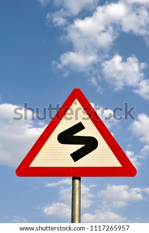  Close up of Red triangle road traffic sign indicating  S Curve  Ahead symbol
as caution,warning  for vehicle driver on highway against blue sky with clouds background,India

