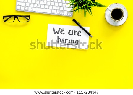 Search for worker, employee concept. We are hiring lettering on work desk on yellow background top view copy space