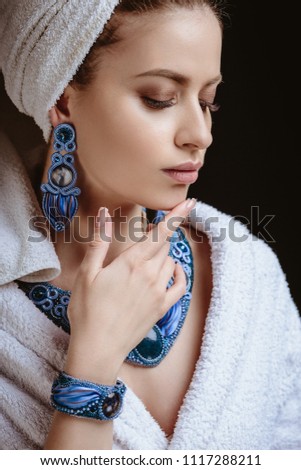 Young woman in a bathrobe and towel on her head, fashion jewelry, spa and care portrait, clean natural face, portrait on a dark background
