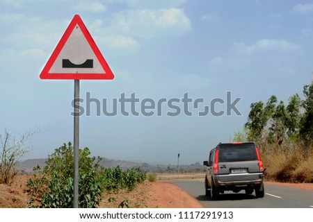  Red triangle  traffic road sign indicating            symbol  of Dangerous Dip Ahead  for vehicle driveas caution,warning 
against blue sky and landscape background ,India