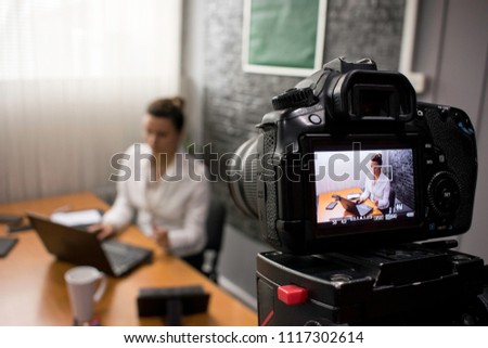 Video camera shoots a young businesswoman sitting at a table in front of a laptop  Royalty-Free Stock Photo #1117302614