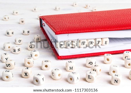 Word Private written in wooden blocks in red notebook on white wooden table. Wooden abc.