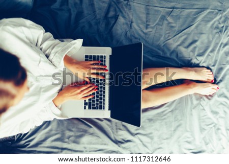 Cropped image of woman using laptop and lying on bed. Top view.Young woman at home in bed typing on laptop. Girl blogger is typing for a fresh post. Staylish toned image