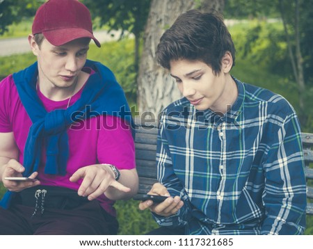 two young brothers in casual sitting on the bench and chatting using their smarphone vintage toned